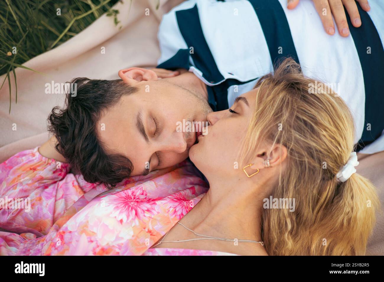 Un couple aimant profite d'un moment romantique à l'extérieur, allongé sur une couverture dans l'herbe. Leur baiser tendre et leur posture détendue reflètent l'amour, l'intimité, et Banque D'Images