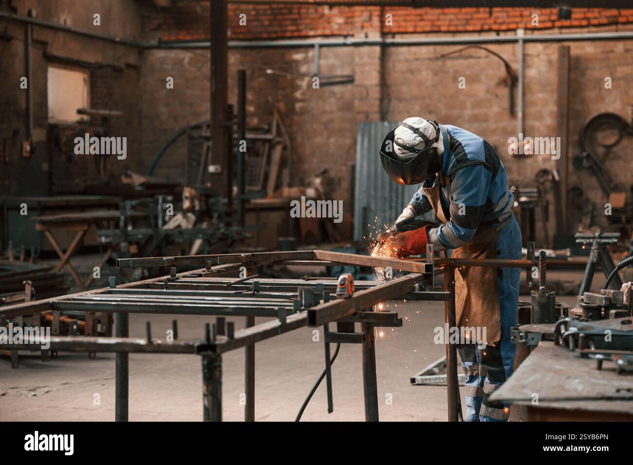 Le travailleur d'usine dans le masque de protection soude le fer. Banque D'Images