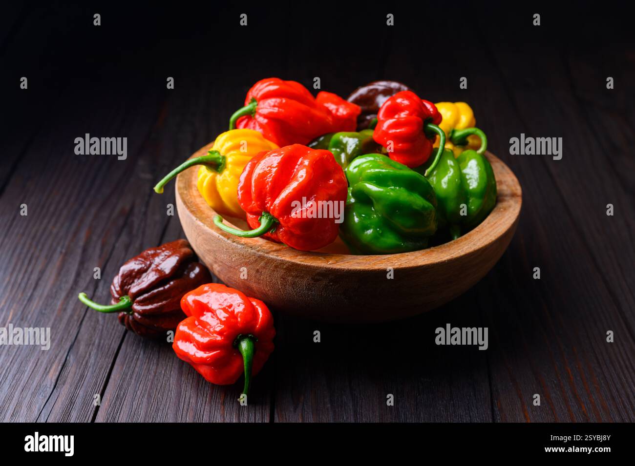 Assiette en bois remplie de poivrons habanero multicolores (capsicum chinense) sur table en bois rustique. Poivrons mexicains très chauds Banque D'Images