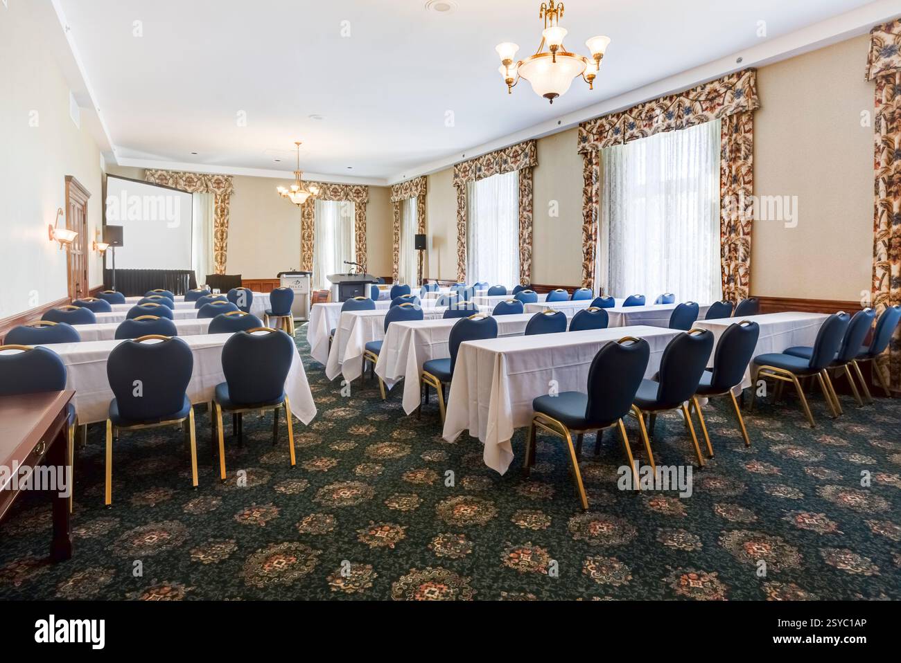 Grande chambre avec de nombreuses chaises et tables. Les chaises sont bleues et les tables sont blanches. Il y a aussi quelques écrans sur les murs Banque D'Images