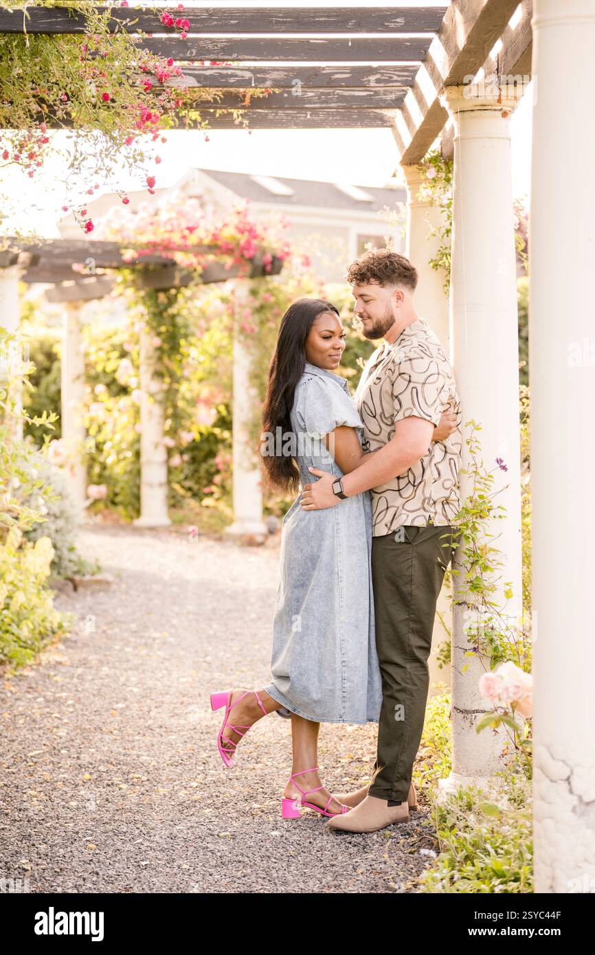 Couple romantique embrassant sous une pergola couverte de fleurs Banque D'Images Couple romantique embrassant sous une pergola couverte de fleurs Banque D'Images