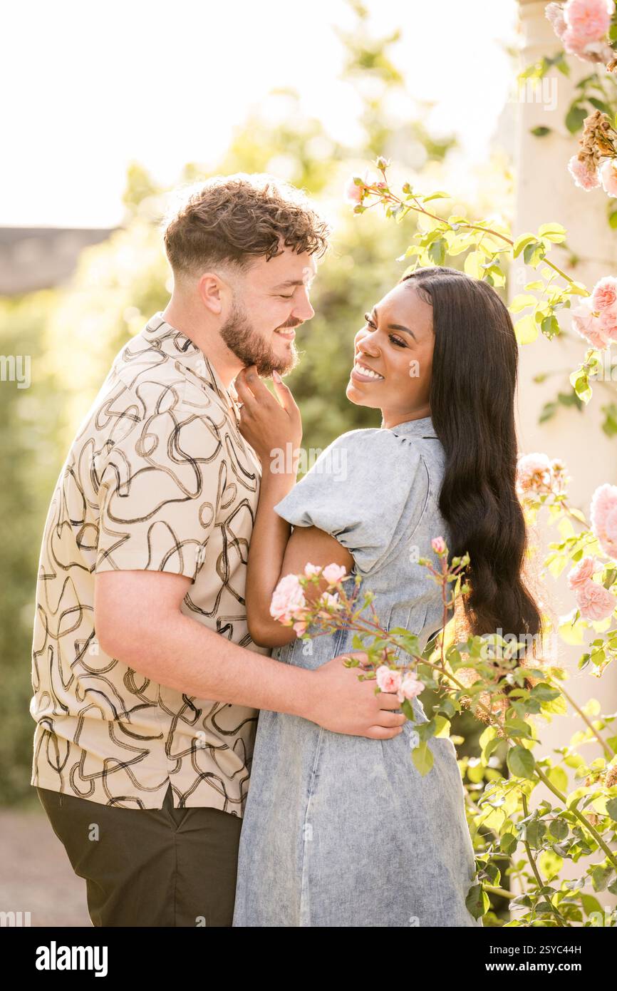 Couple souriant embrassant dans un jardin ensoleillé Banque D'Images Couple souriant embrassant dans un jardin ensoleillé Banque D'Images