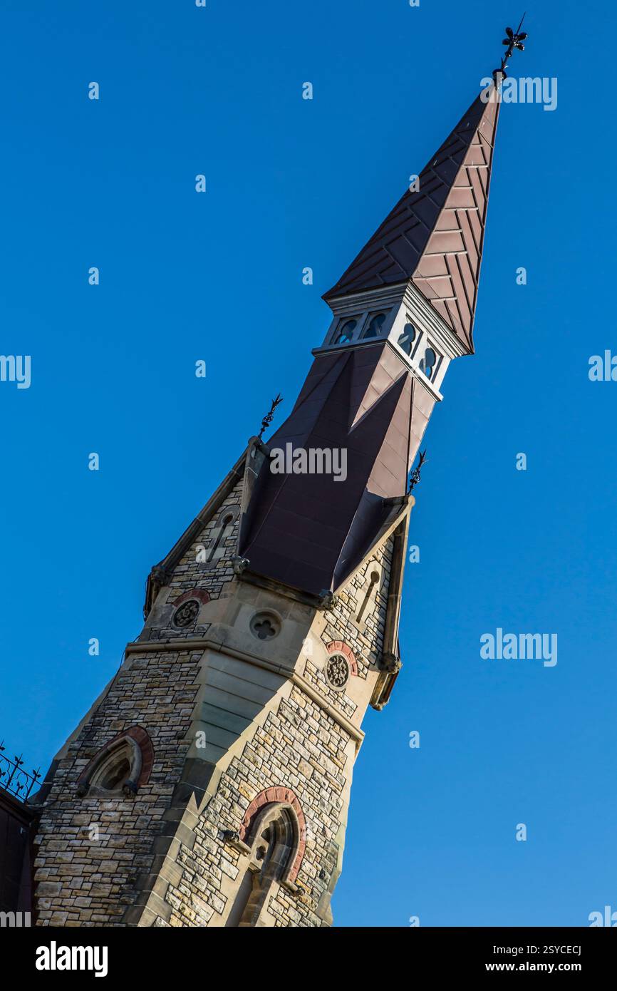 Grand bâtiment en briques avec un clocher. Le bâtiment est brun et a un toit pointu. Le ciel est bleu et clair Banque D'Images