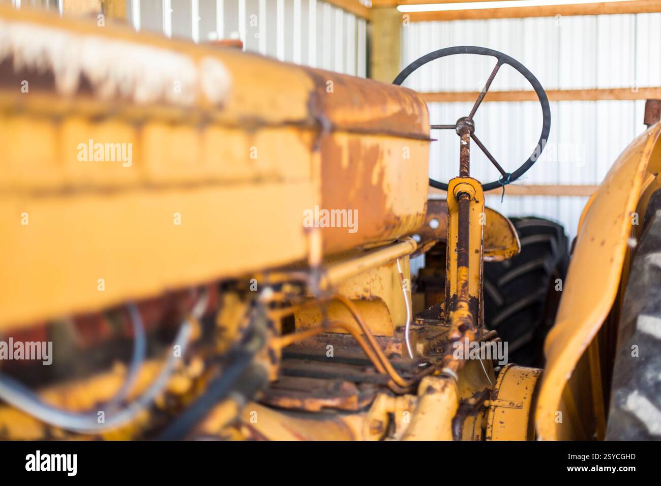 Tracteur jaune avec volant rouillé. Le tracteur est garé dans une grange Banque D'Images