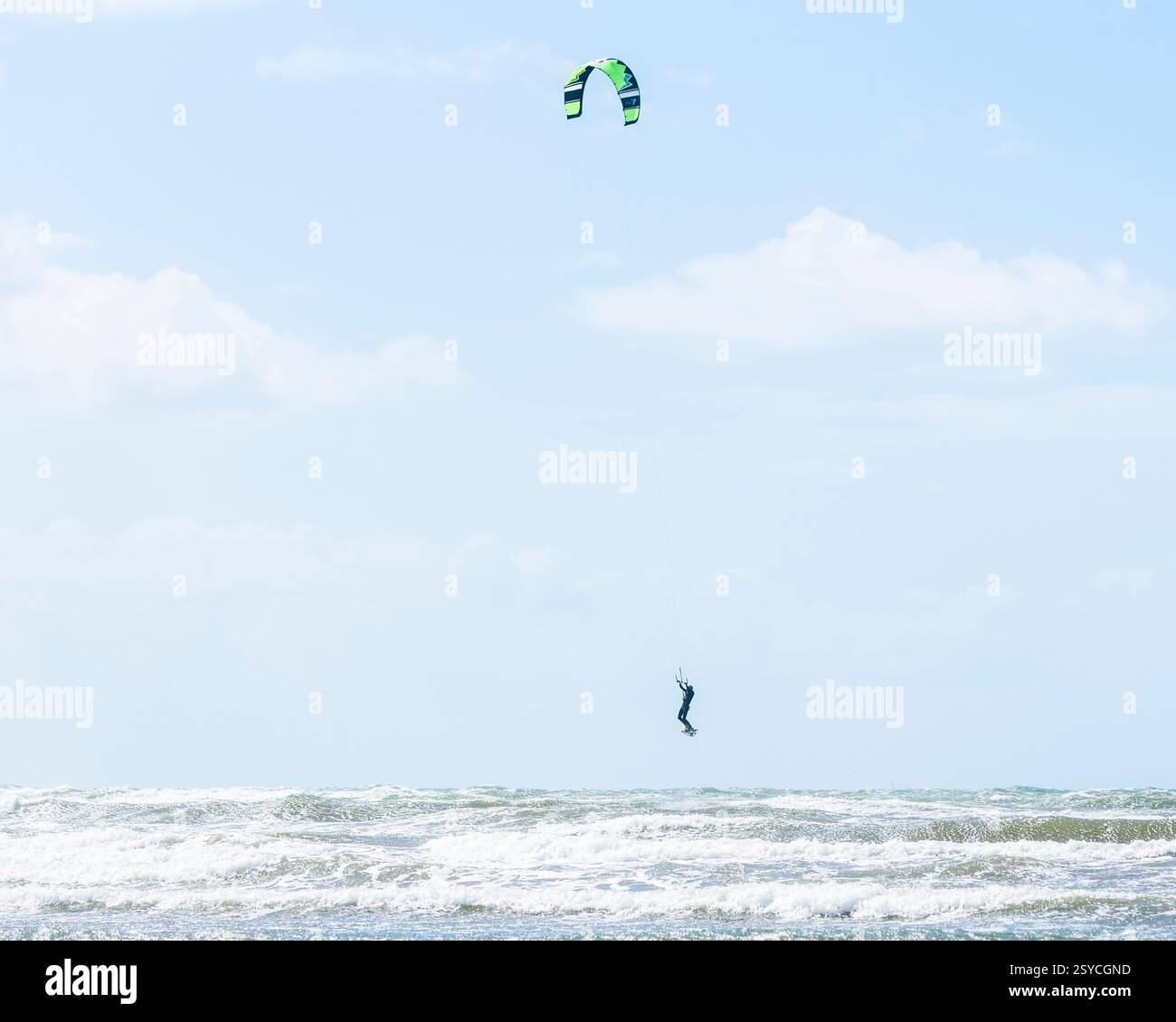 Un kitesurfer habile navigue sur les vagues énergiques de la côte suédoise sous un ciel bleu clair. Le soleil d'été améliore la scène vibrante comme le cerf-volant Banque D'Images