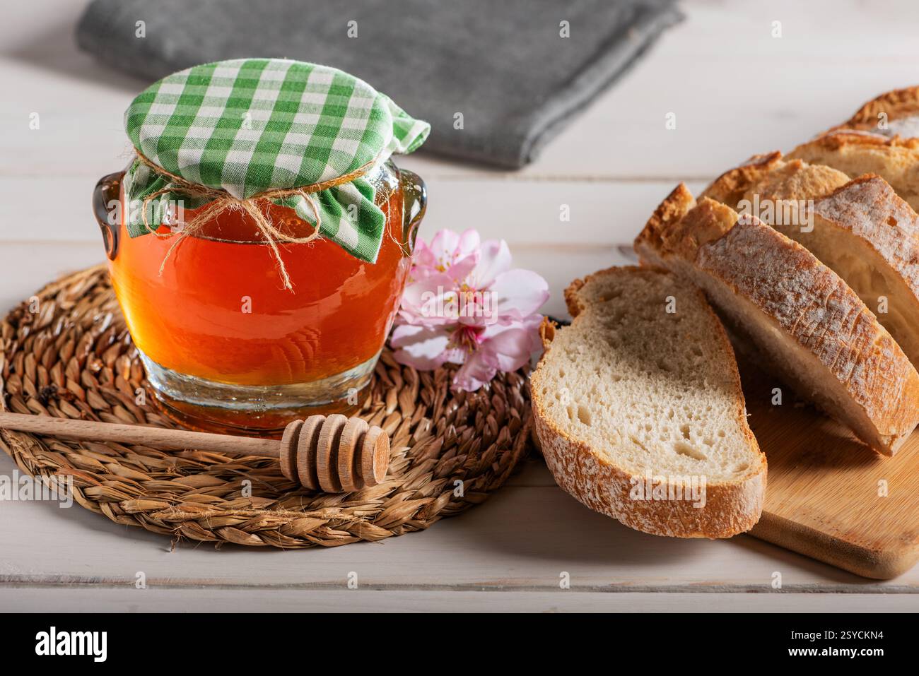 Bocal en verre avec du miel d'abeille à côté d'une trempette de miel, quelques fleurs d'amandes et des tranches de pain. Banque D'Images