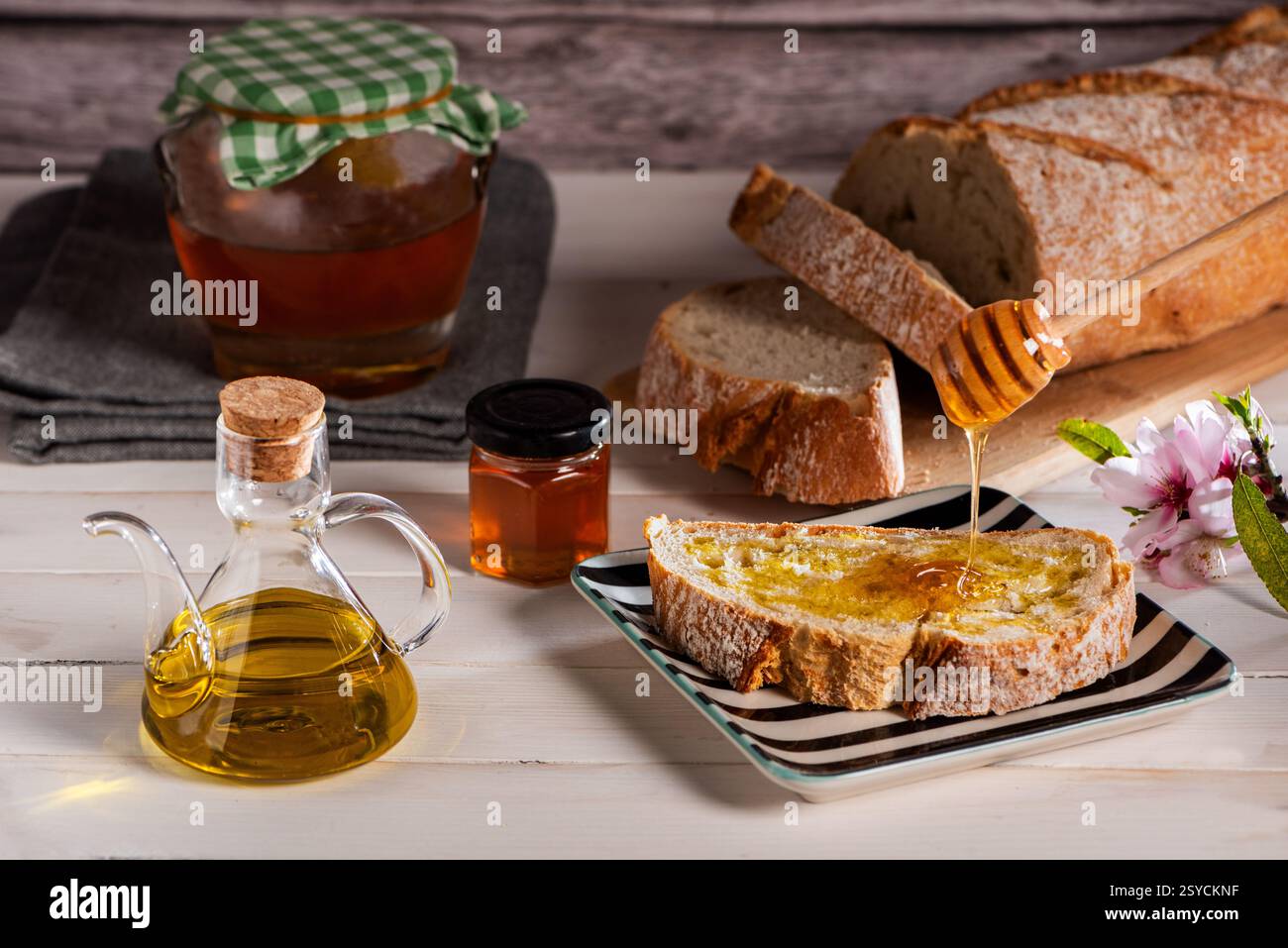 Tranche de pain grillée avec de l'huile d'olive et du miel, sur une table blanche avec un distributeur d'huile, un pot de miel, et une miche de pain tranchée. Banque D'Images