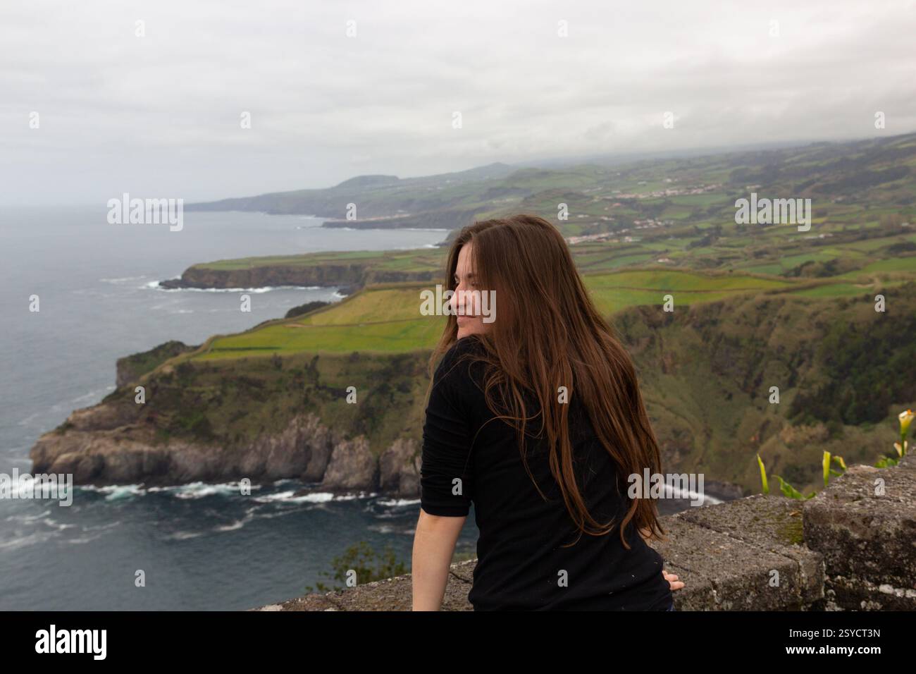 Une jeune femme aux longs cheveux roux regarde la vue imprenable sur l'océan dans les îles des Açores, au Portugal. Le littoral accidenté et l'Atlantique bleu profond créent Banque D'Images