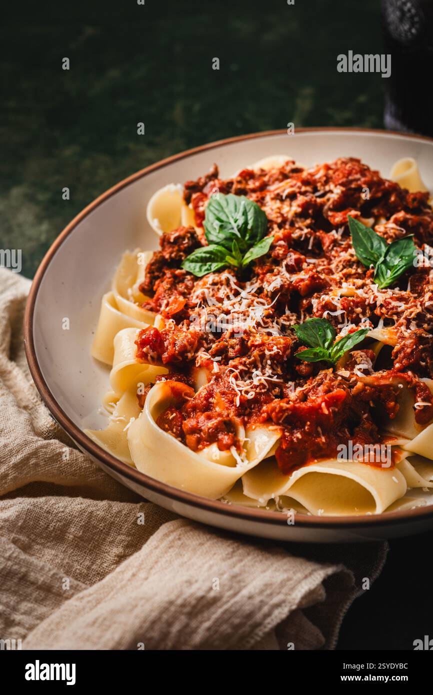 Un plat copieux de pâtes pappardelle avec une riche sauce à la viande bolognaise, garni de feuilles de basilic frais et de parmesan râpé. Banque D'Images