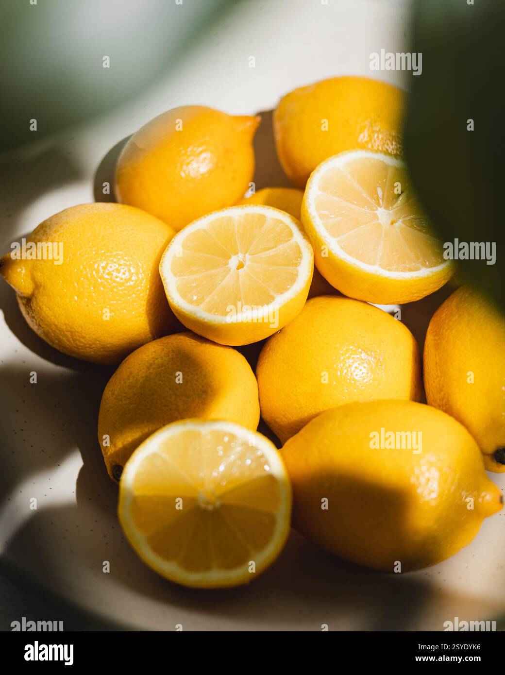 Citrons jaune vif frais avec plusieurs coupés en deux montrant la pulpe juteuse et des segments sur une toile de fond de citrons entiers. Banque D'Images