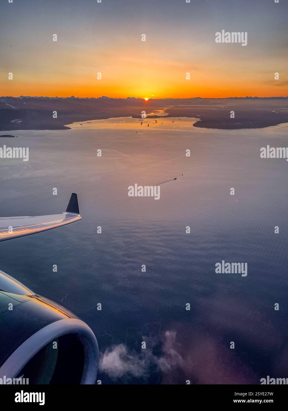 Vue aérienne depuis une fenêtre d'avion d'un océan et des îles au lever du soleil. L'aile de l'avion reflète les teintes dorées de la lumière matinale au-dessus du - Image de stock capturée avec un smartphone