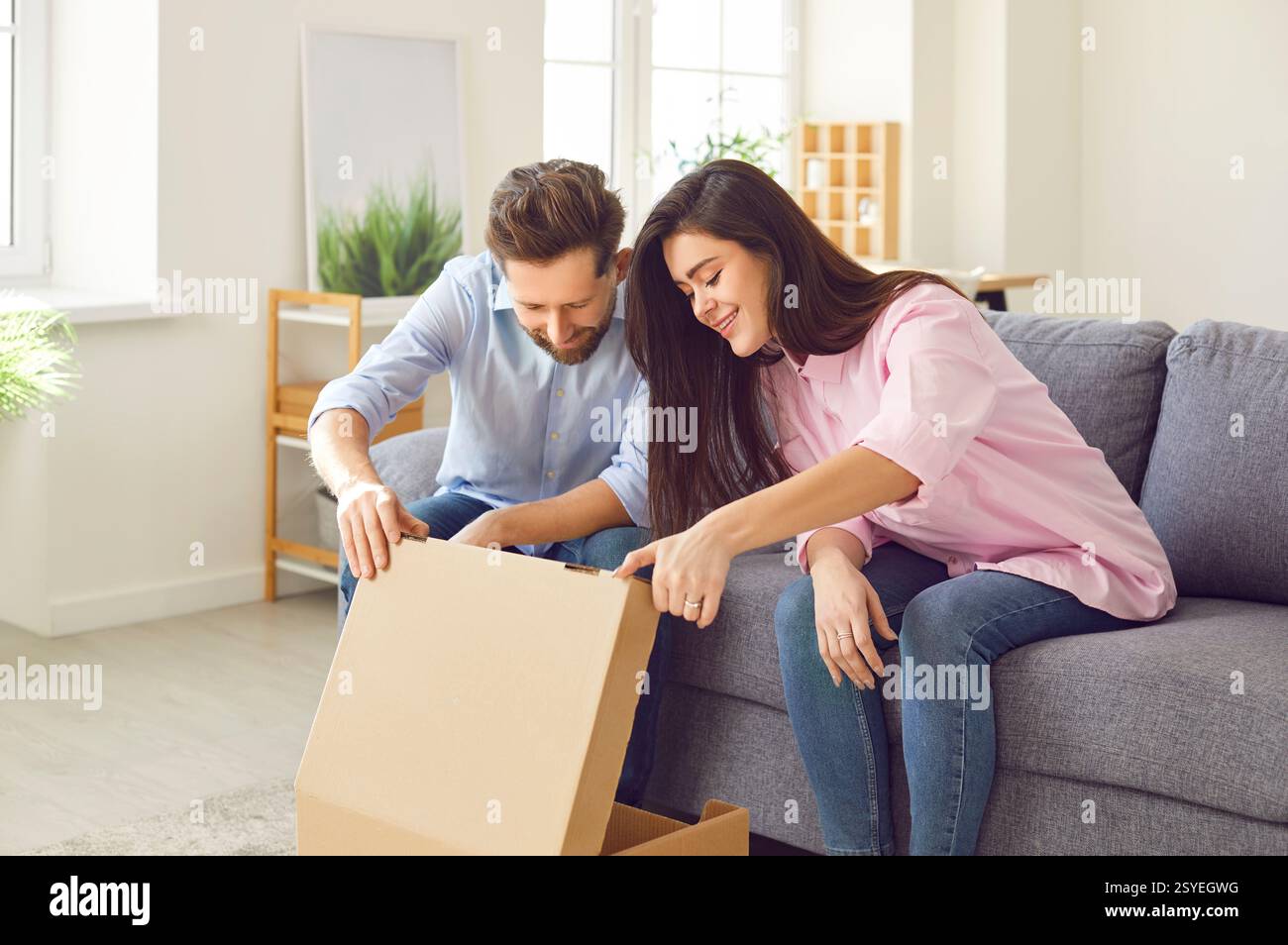 Couple regarde joyeusement et avec attente à l'intérieur de la boîte en carton ouverte, regardant un nouvel achat ou un cadeau. Banque D'Images