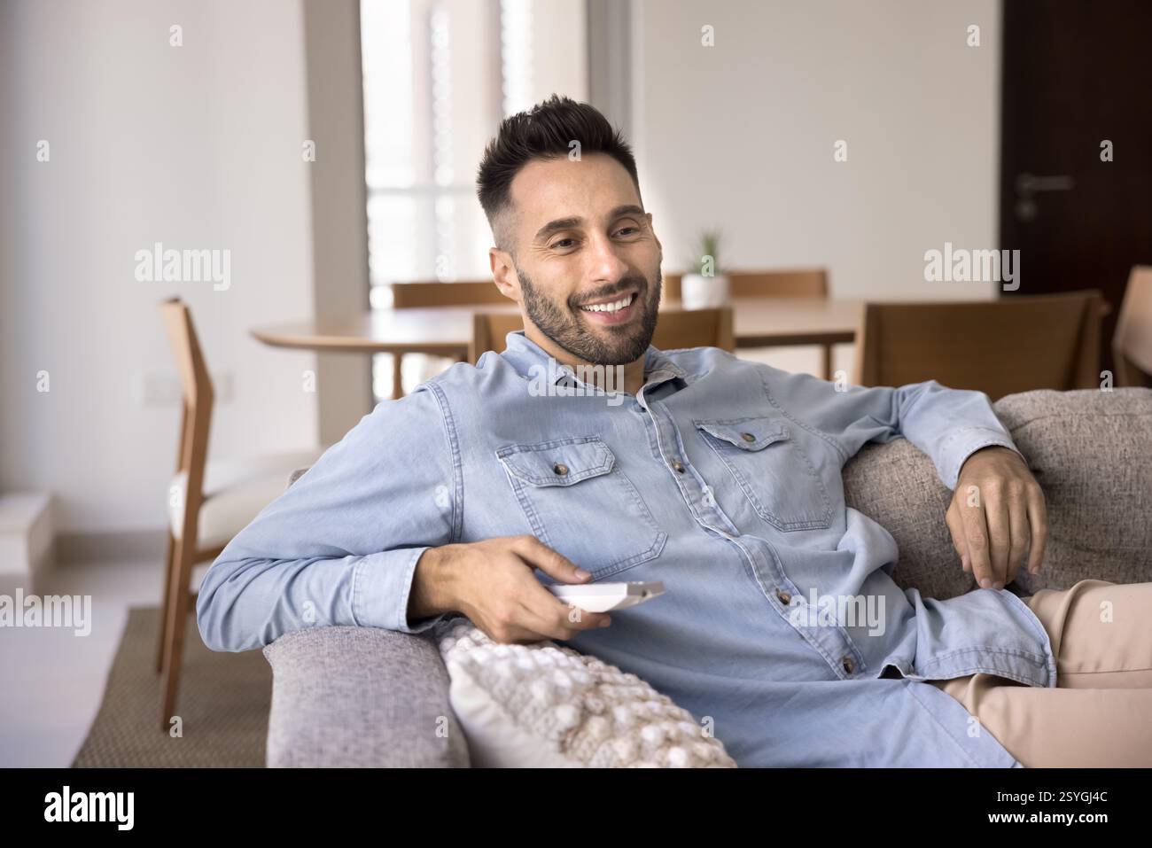 Homme hispanique simple se relaxant sur le canapé avec télécommande Banque D'Images