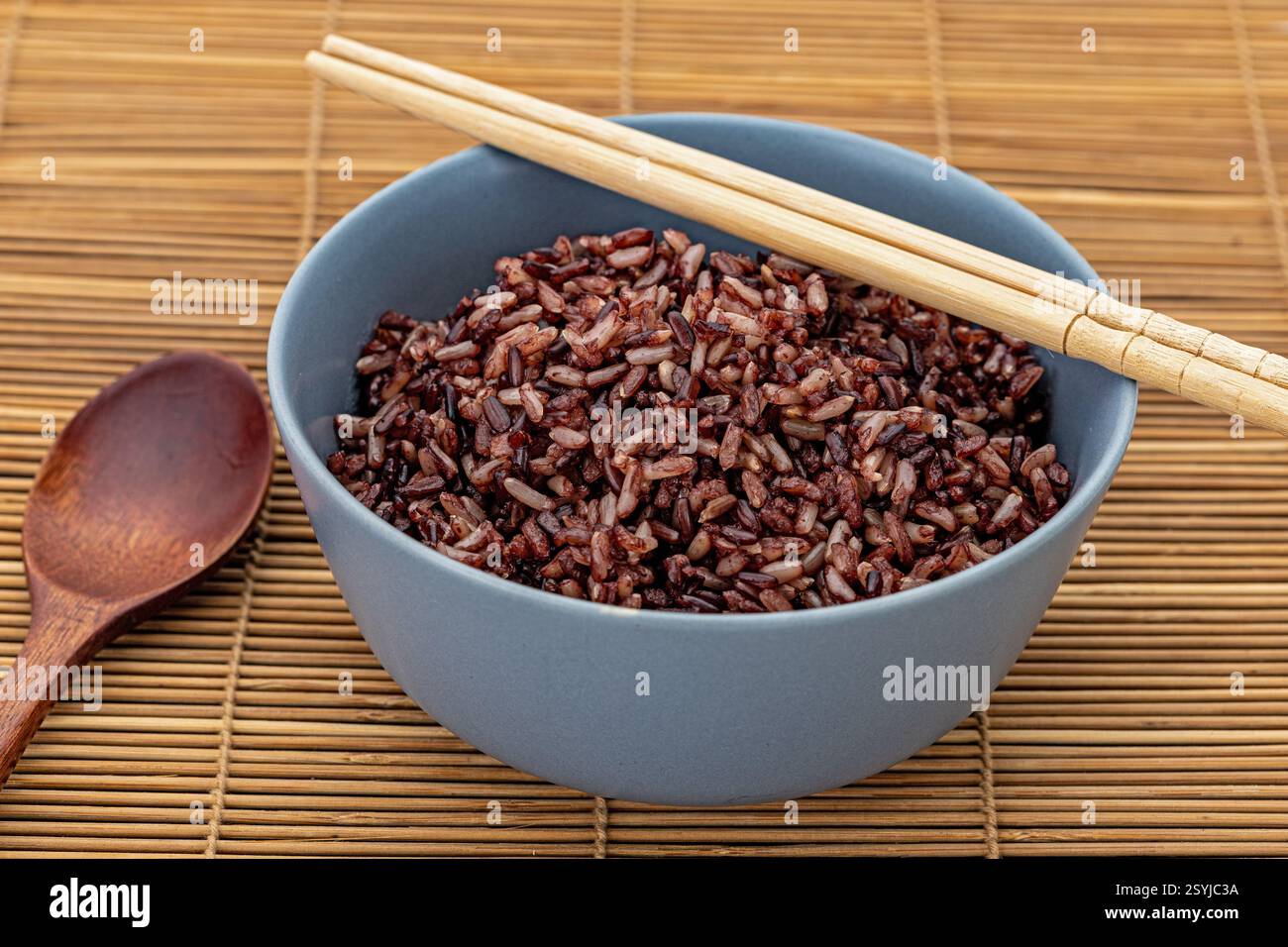 Riz brun cuit sain mélangé à des riceberry dans un bol en céramique grise avec une cuillère en bois et des baguettes en bambou. Banque D'Images