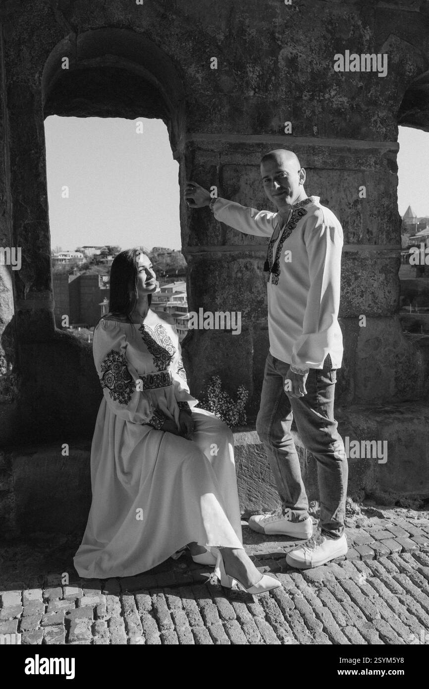 Mariage d'été en Géorgie : couple romantique dans des tenues brodées ukrainiennes embrassant sous une ancienne arche Banque D'Images