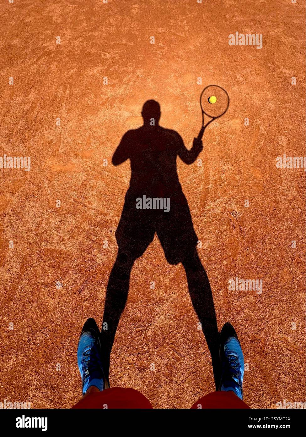Homme jouant au tennis par une journée ensoleillée. Regardant vers le bas à l'ombre d'un joueur de tennis sur un court de terre battue de sable. - Image de stock capturée avec un smartphone