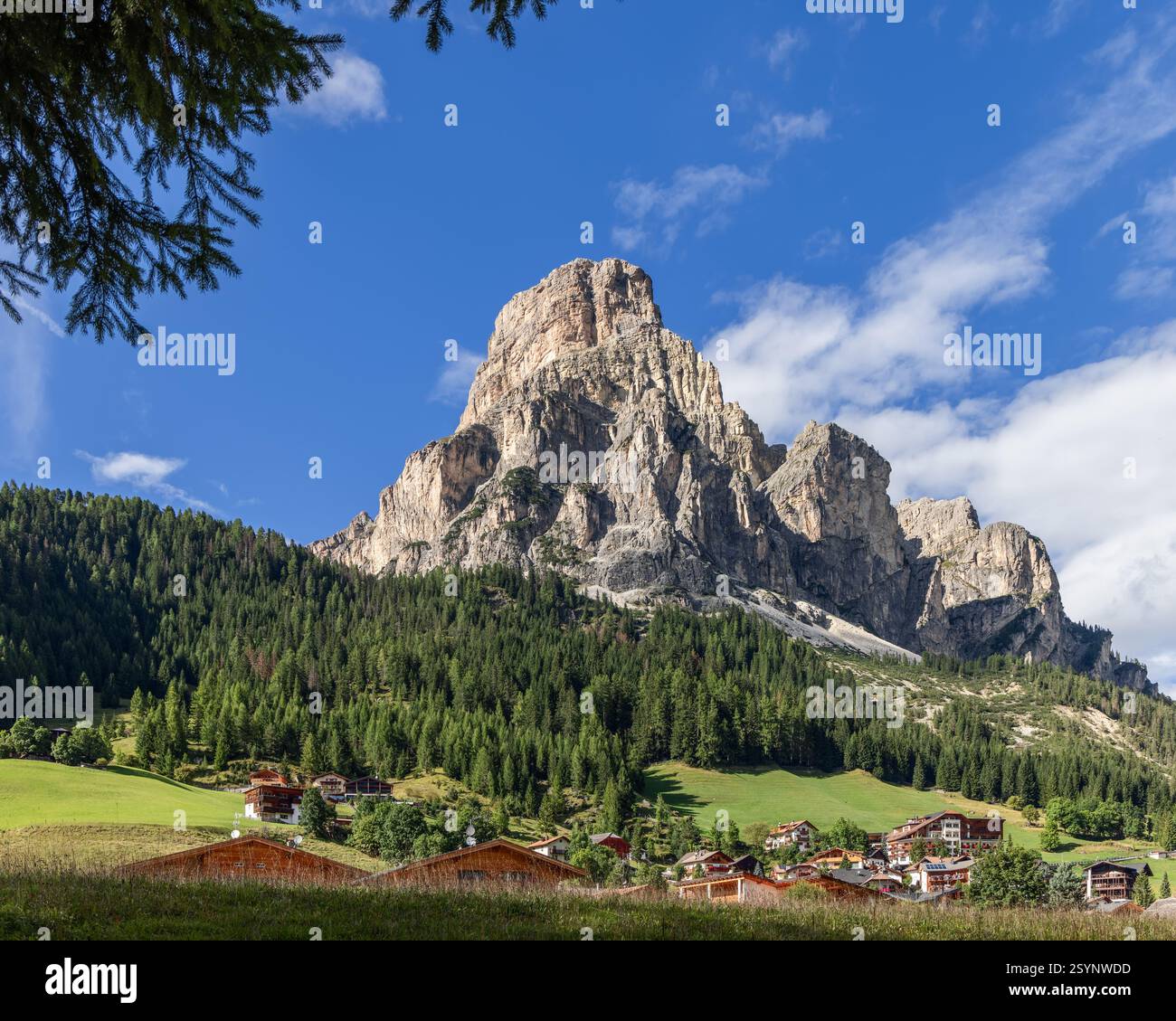 La montagne Sassongher domine le paysage au-dessus de Colfosco, avec des chalets en bois nichés dans des prairies verdoyantes et entourés de forêts Banque D'Images