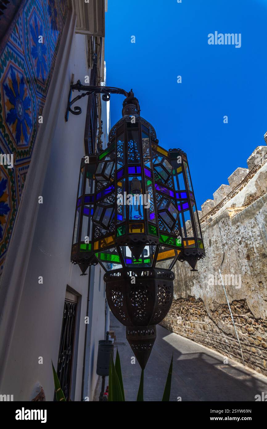 Lanterne marocaine vibrante avec panneaux de vitraux colorés, projetant des ombres complexes contre un mur blanchi à la chaux et ajoutant une touche de couleur vibrante Banque D'Images