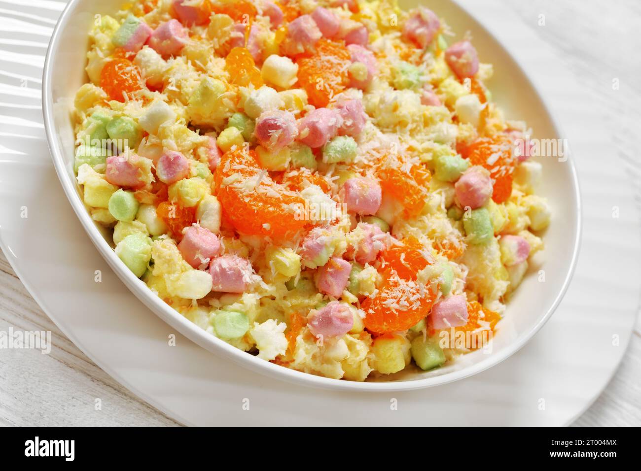 Salade d'Ambrosia à l'ananas, aux mandarines, au yaourt, aux mini guimauves, à la noix de coco et à la crème fouettée dans un bol blanc sur une table en bois blanc, américaine RE Banque D'Images