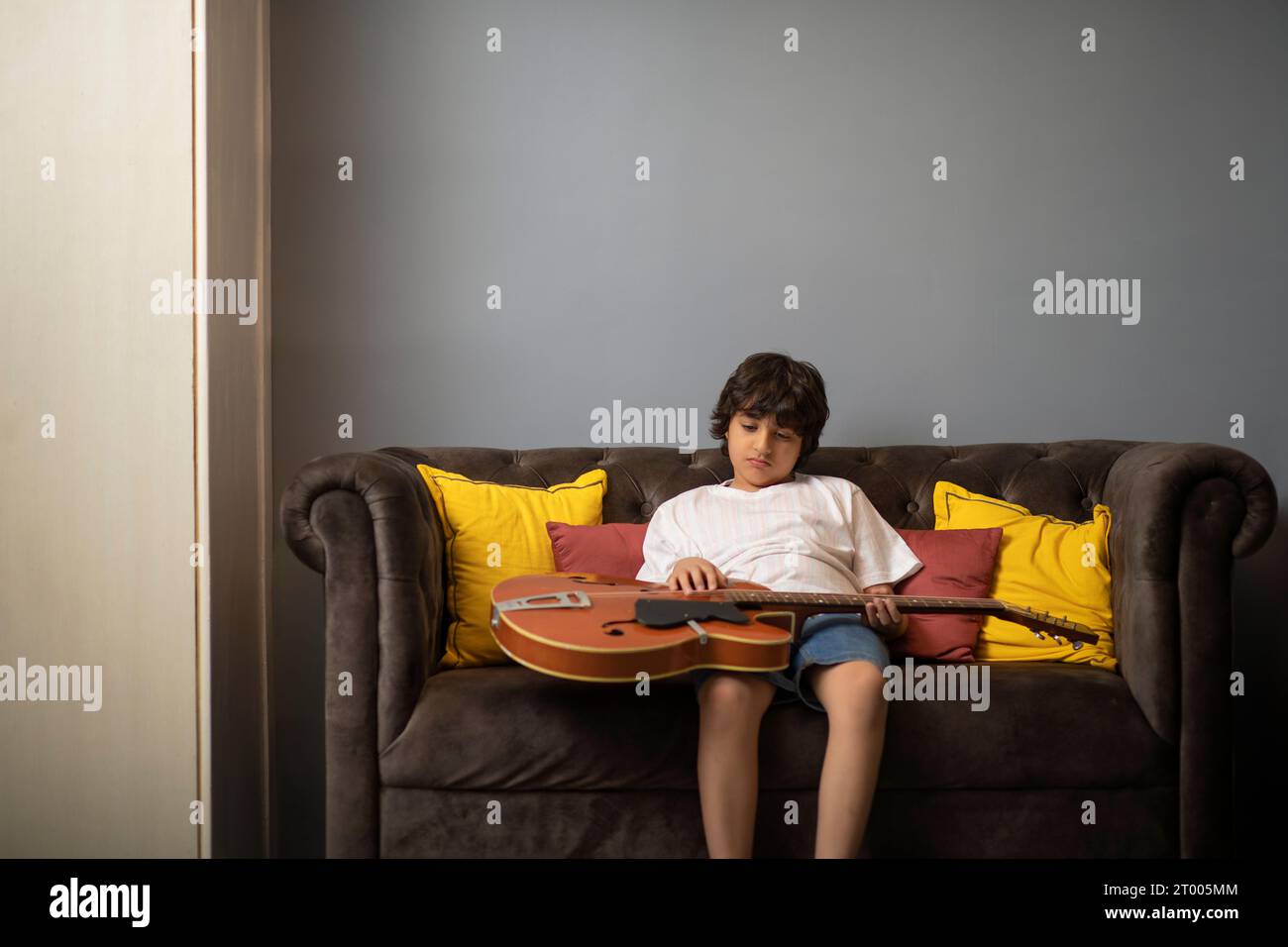 Garçon jouant de la guitare tout en se penchant sur le canapé dans le salon Banque D'Images