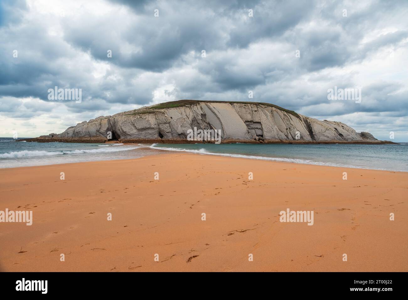 Isla del Castro avec plage de sable de Covachos, Santander, Cantabrie, Espagne. Île rocheuse et broche sablonneuse par jour nuageux de mauvaise humeur. Destination de voyage populaire Banque D'Images
