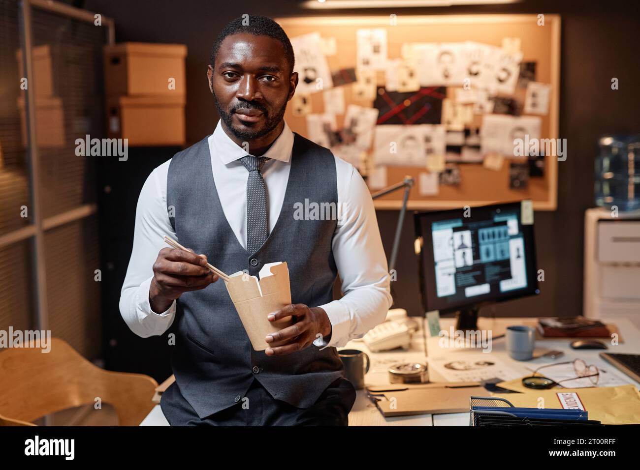 Portrait de jeune homme noir comme détective mangeant des nouilles à emporter dans le bureau et regardant la caméra, l'espace de copie Banque D'Images