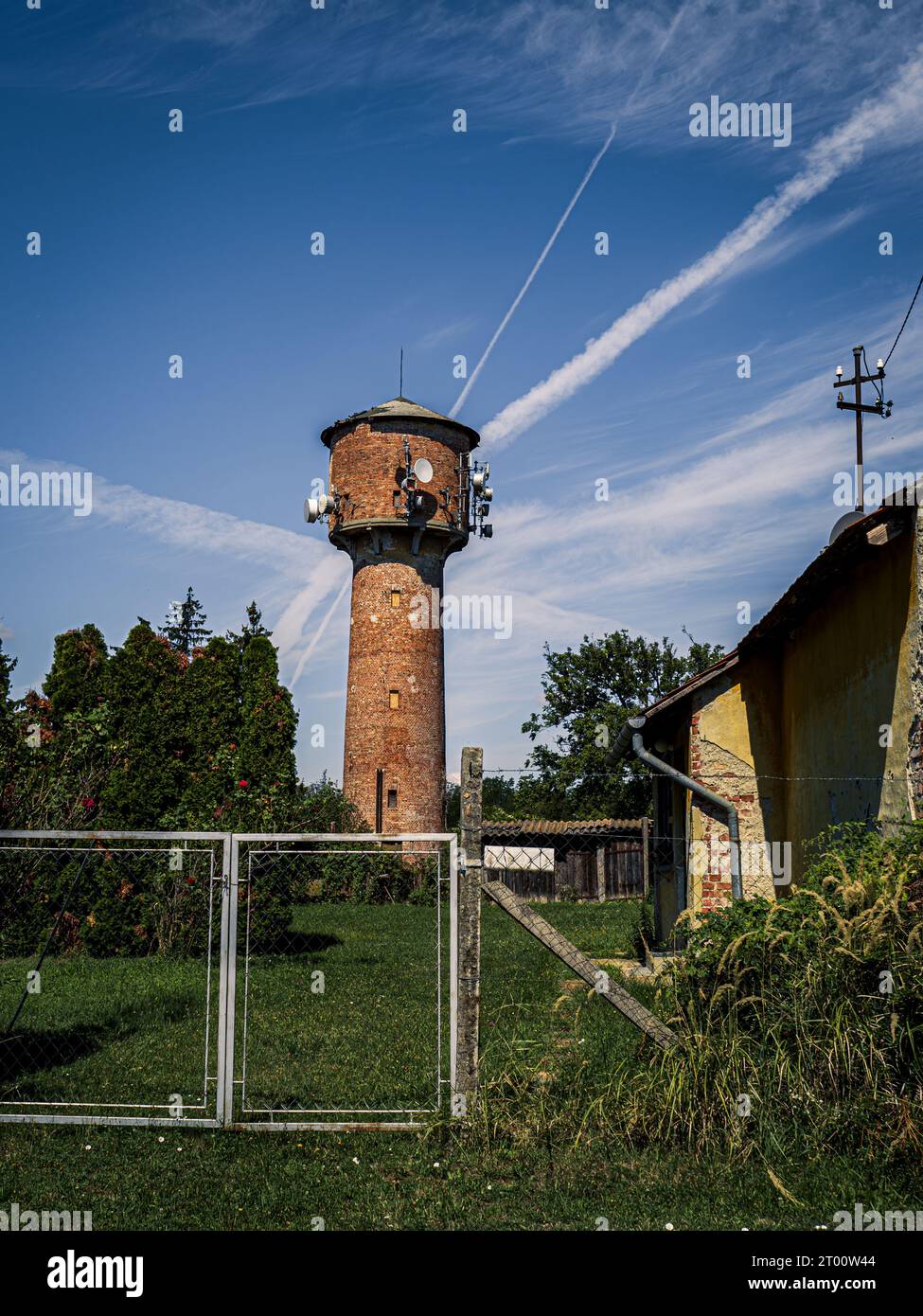 Brique vieux château d'eau avec équipement de télécommunications dans un cadre rural à côté d'un arbre de champ vert ferme ciel nuageux bleu Banque D'Images