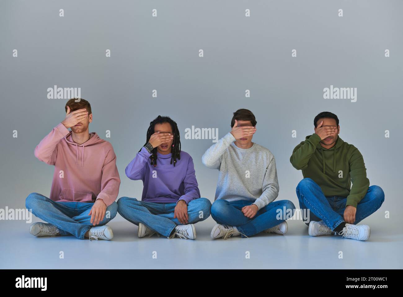 hommes multiculturels dans des tenues à la mode assis avec les jambes croisées couvrant les yeux avec les mains, la diversité Banque D'Images