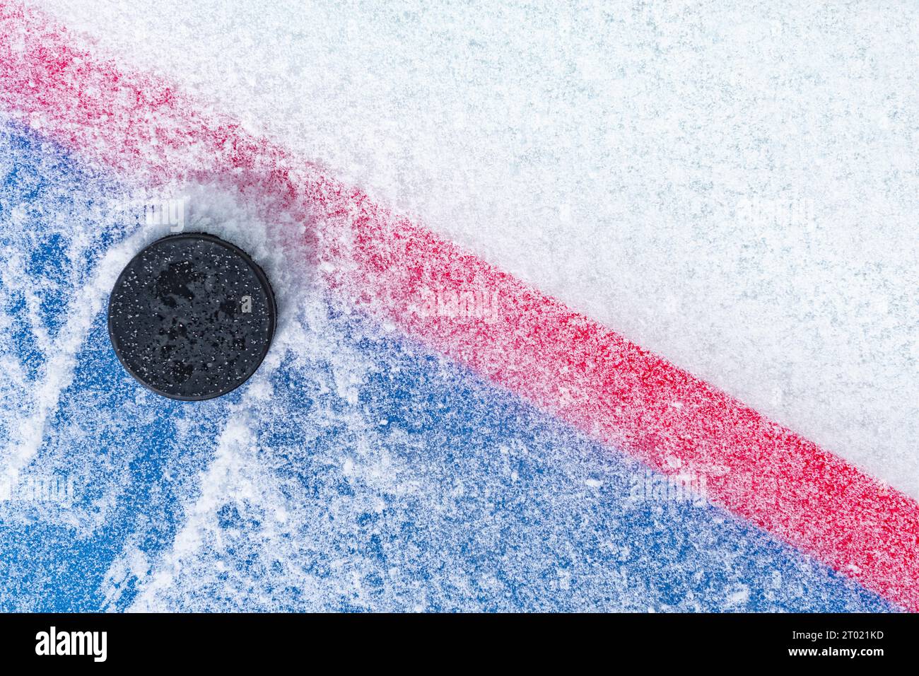 Regardant vers le bas sur un palet de hockey sur glace noir labourant à travers la neige et s'arrêtant sur le bord de la ligne de but du pli de but. Banque D'Images