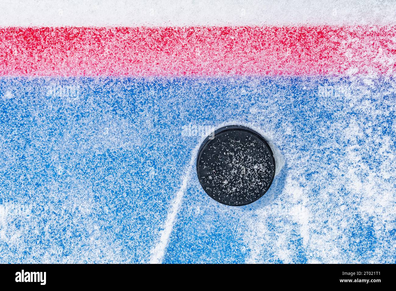 Regardant vers le bas sur un palet de hockey sur glace noir labourant à travers la neige et s'arrêtant sur le bord de la ligne de but du pli de but. Banque D'Images