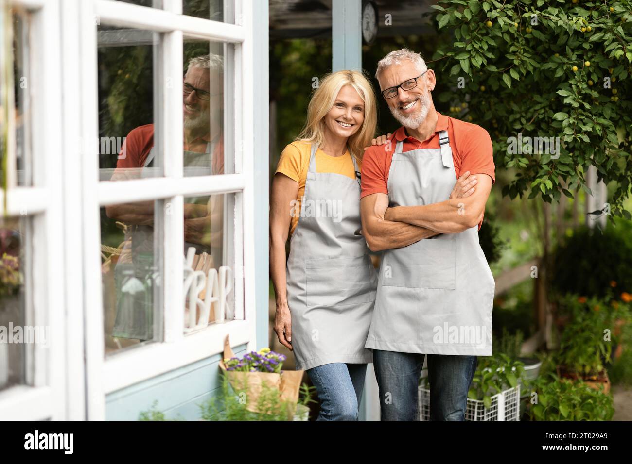 Heureux couple de fermiers matures portant des tabliers posant ensemble à Terrace Outdoors Banque D'Images