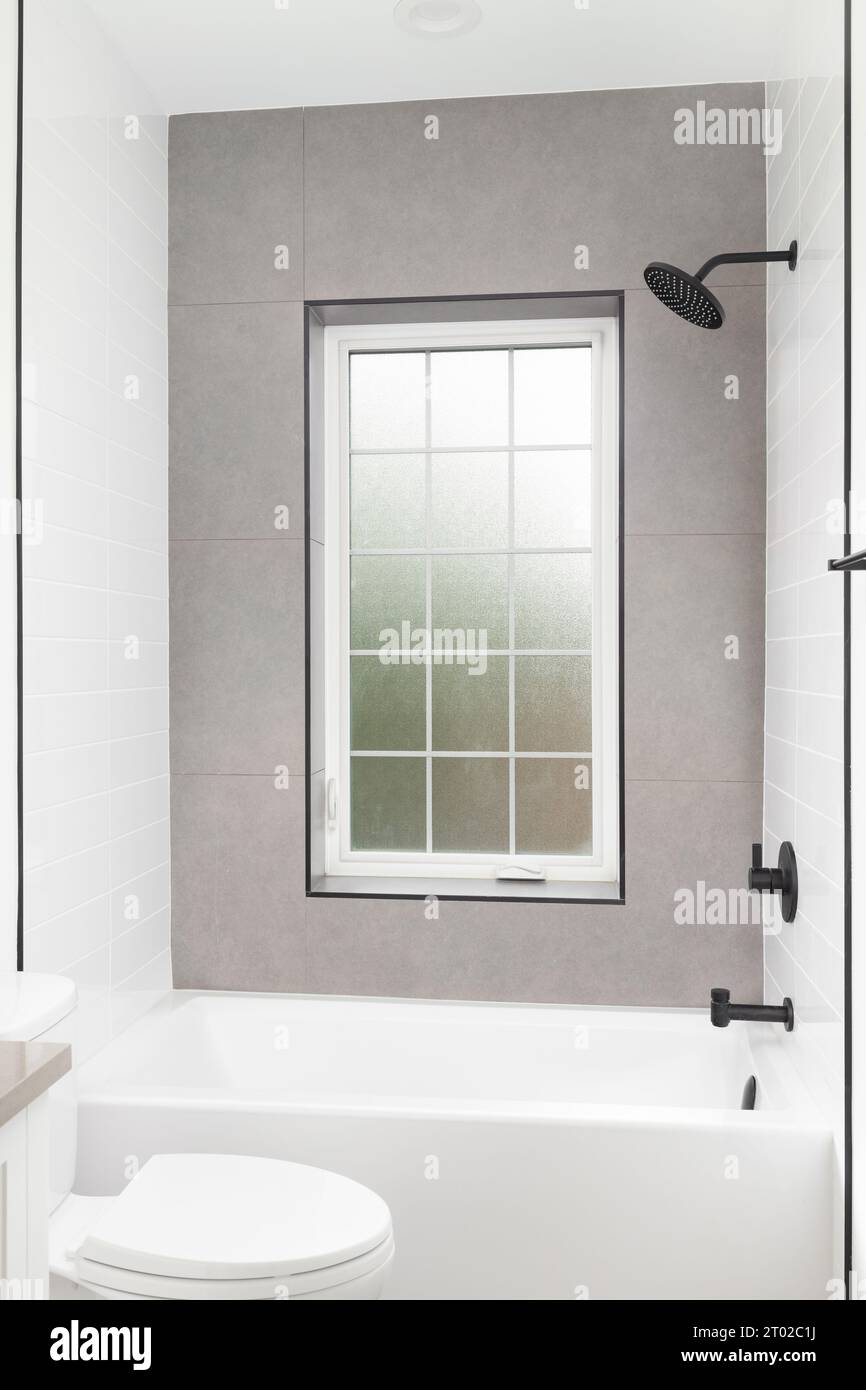 Une douche de luxe avec métro blanc et murs de carreaux bruns, robinet noir, et une fenêtre encadrée blanche avec verre dépoli. Banque D'Images