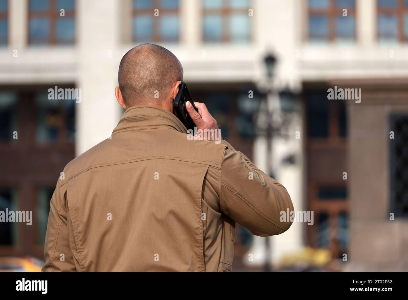 Homme avec la tête rasée parlant sur un téléphone portable dans une rue de la ville. Concept de communication cellulaire Banque D'Images