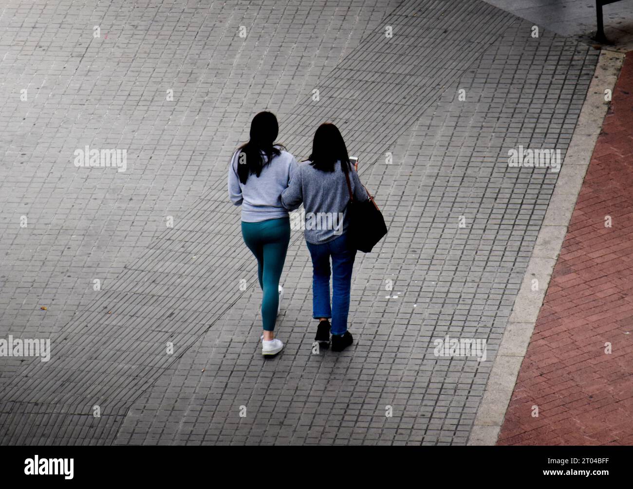 Vue arrière de deux jeunes femmes marchant ensemble sur le trottoir d'une rue par temps gris. Banque D'Images