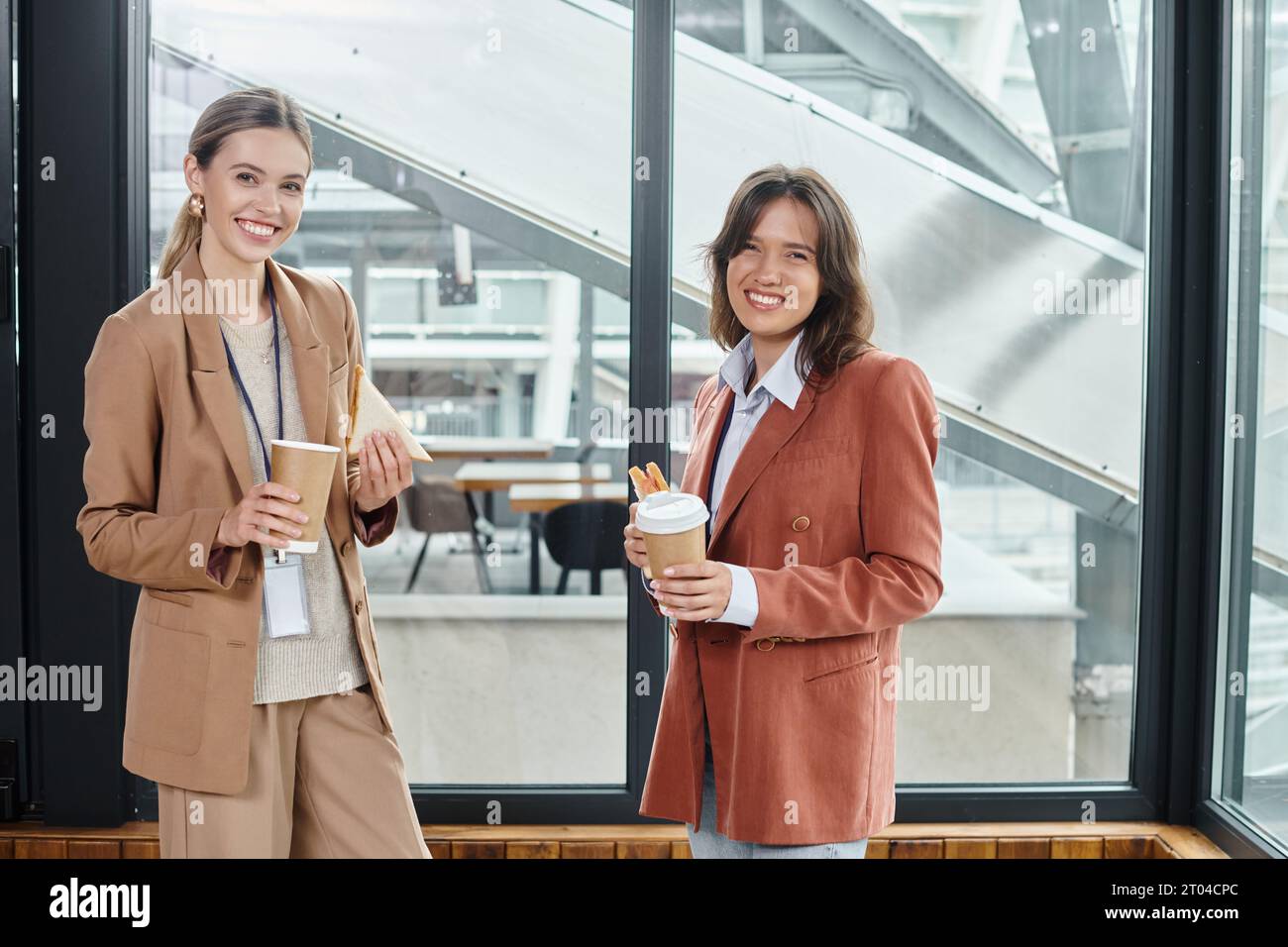 collègues élégants dans des tenues décontractées d'affaires souriant et appréciant le café et les sandwichs, coworking Banque D'Images