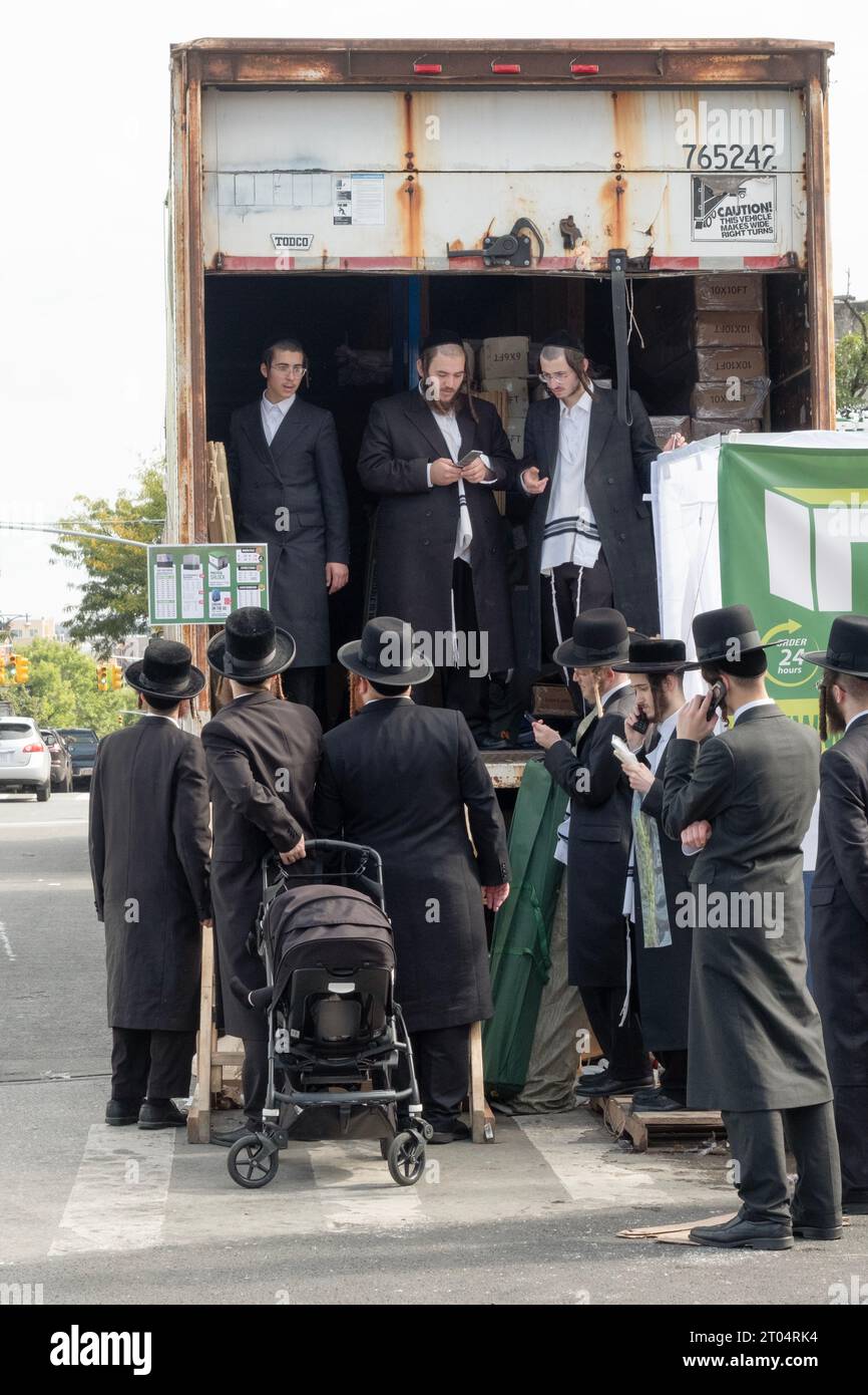 Un groupe d'hommes juifs orthodoxes se tiennent à côté d'une grande ruck attendant d'acheter préfabriqués et faites-le vous-même Sukkahs. À Williamsburg, Brooklyn, New York. Banque D'Images
