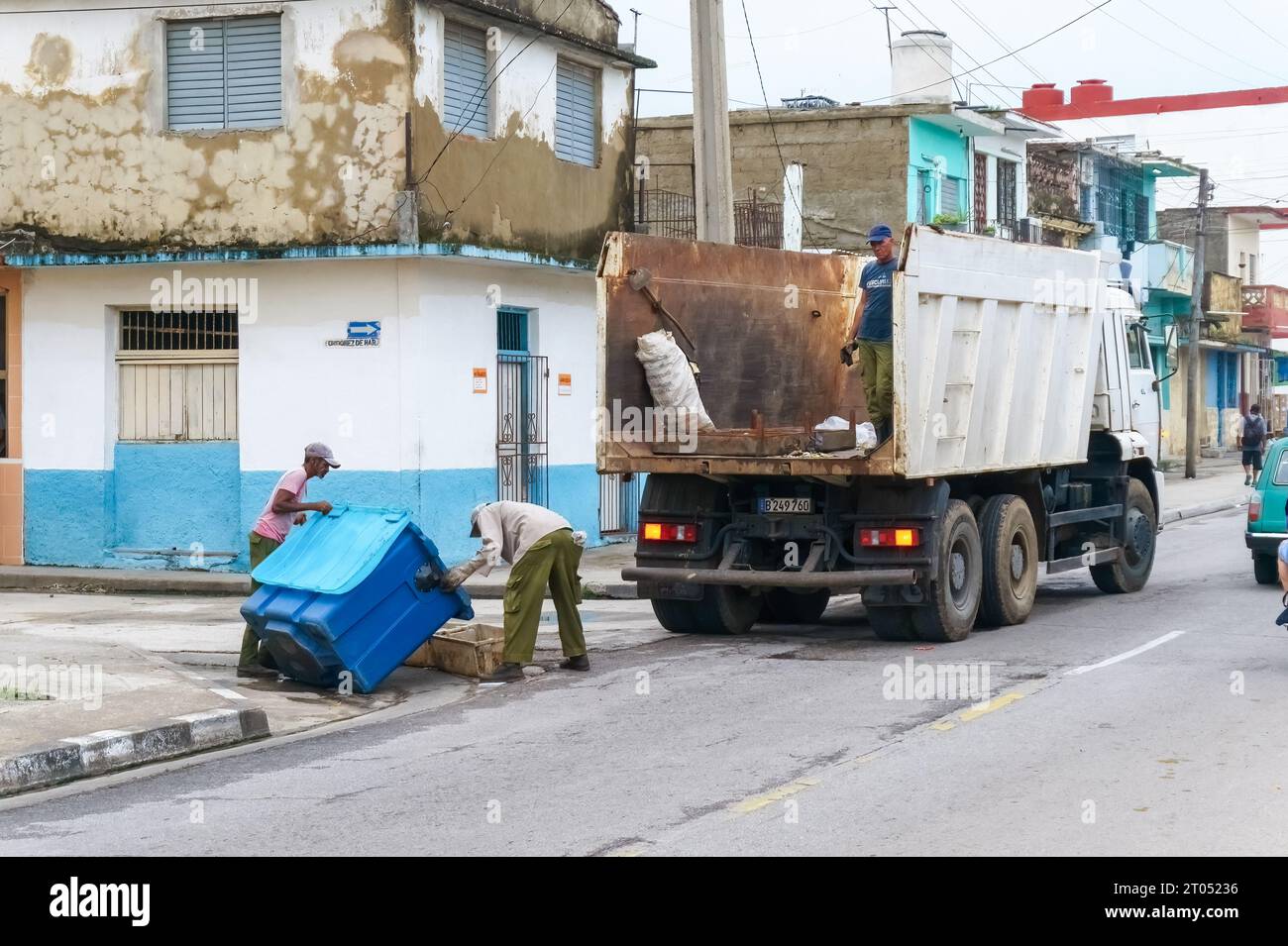 Hommes cubains travaillant dans la collecte des ordures dans une rue de la ville. Ils tournent le grand bac pour enlever manuellement les ordures avec de la houe avant de les charger sur un camion Banque D'Images