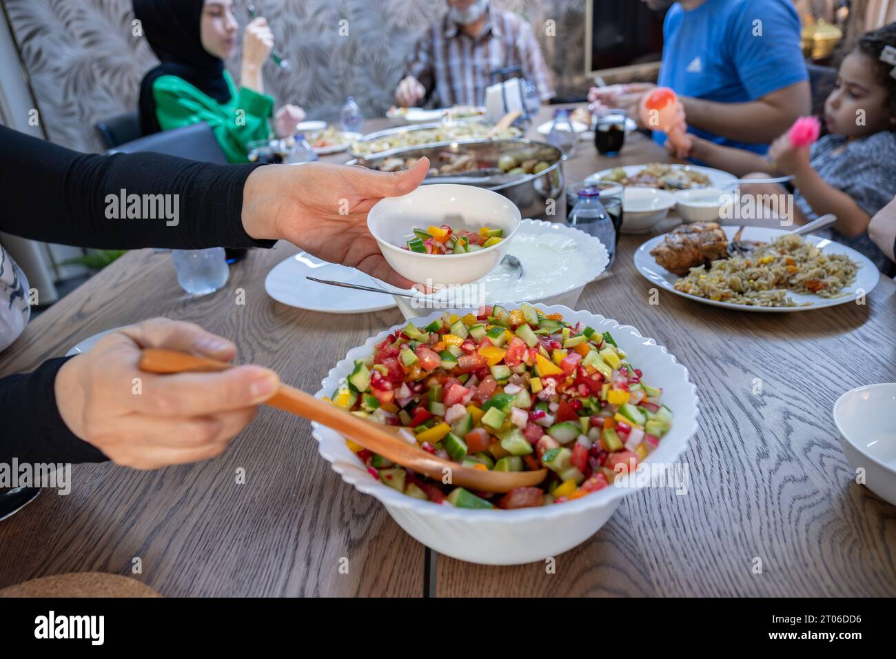 La femme remplit un saladier avec un grand bol de yaourt à côté pour fournir aux invités ce dont ils ont besoin à l'heure du déjeuner au grand tabl collectif Banque D'Images