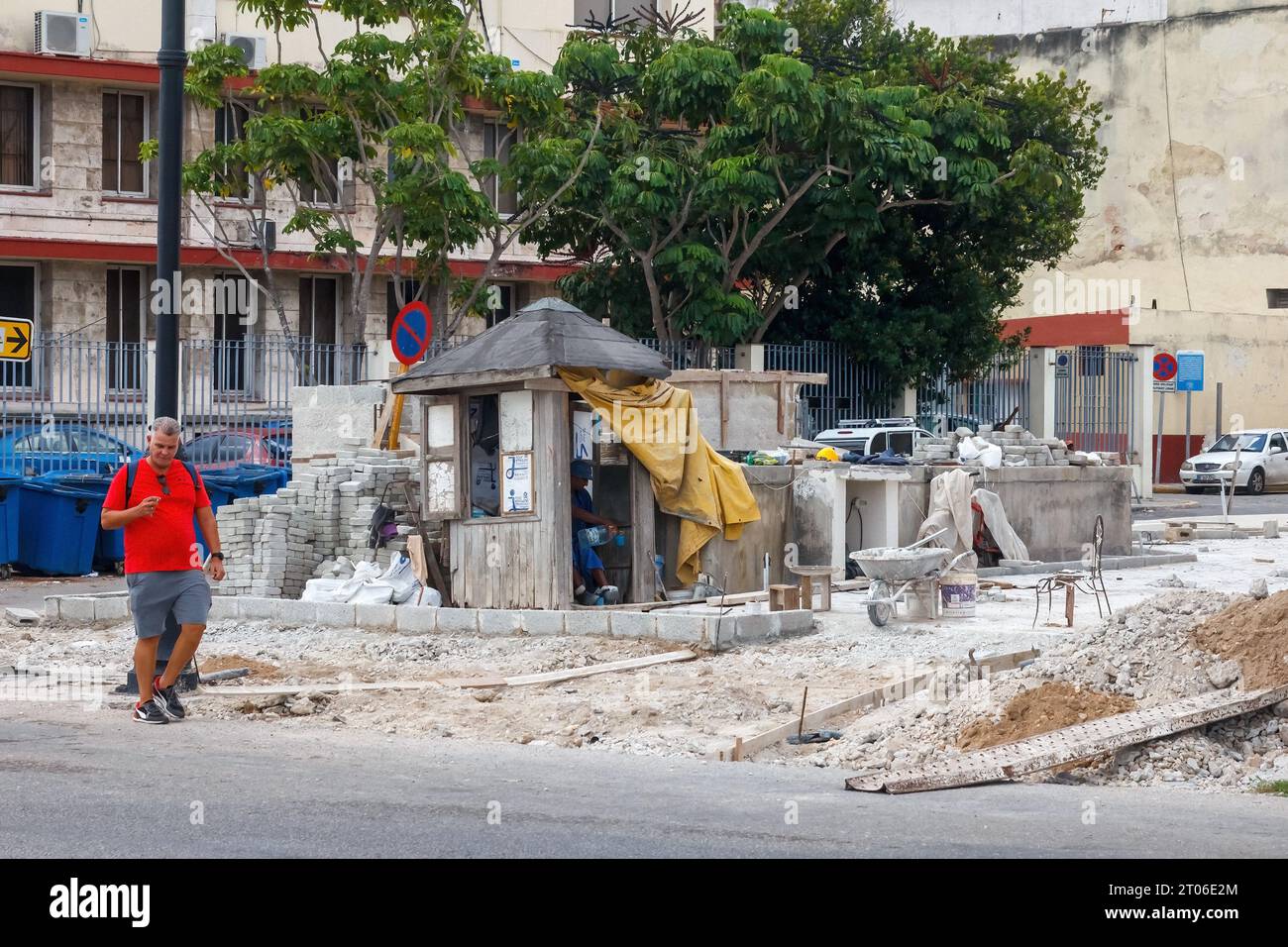 Un cubain marche dans une rue de la ville. À droite, un bâtiment effondré est en cours de reconstruction. Il y a une cabine de sécurité rustique dans le coin Banque D'Images
