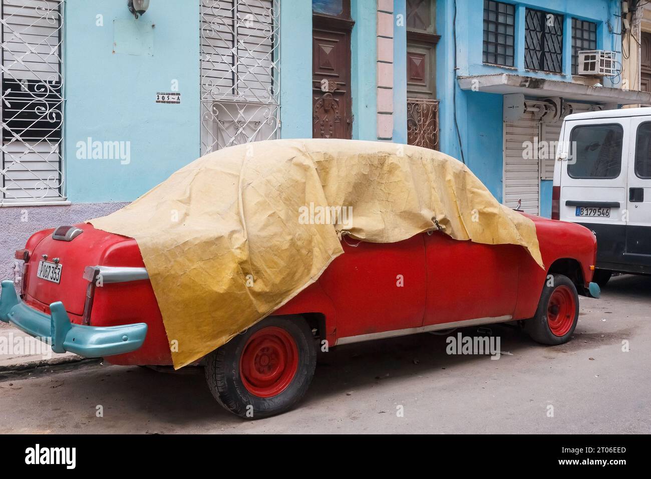 Une voiture américaine vintage rouge est recouverte d'une bâche. Le véhicule à moteur est stationné à l'extérieur des anciens bâtiments résidentiels. Banque D'Images