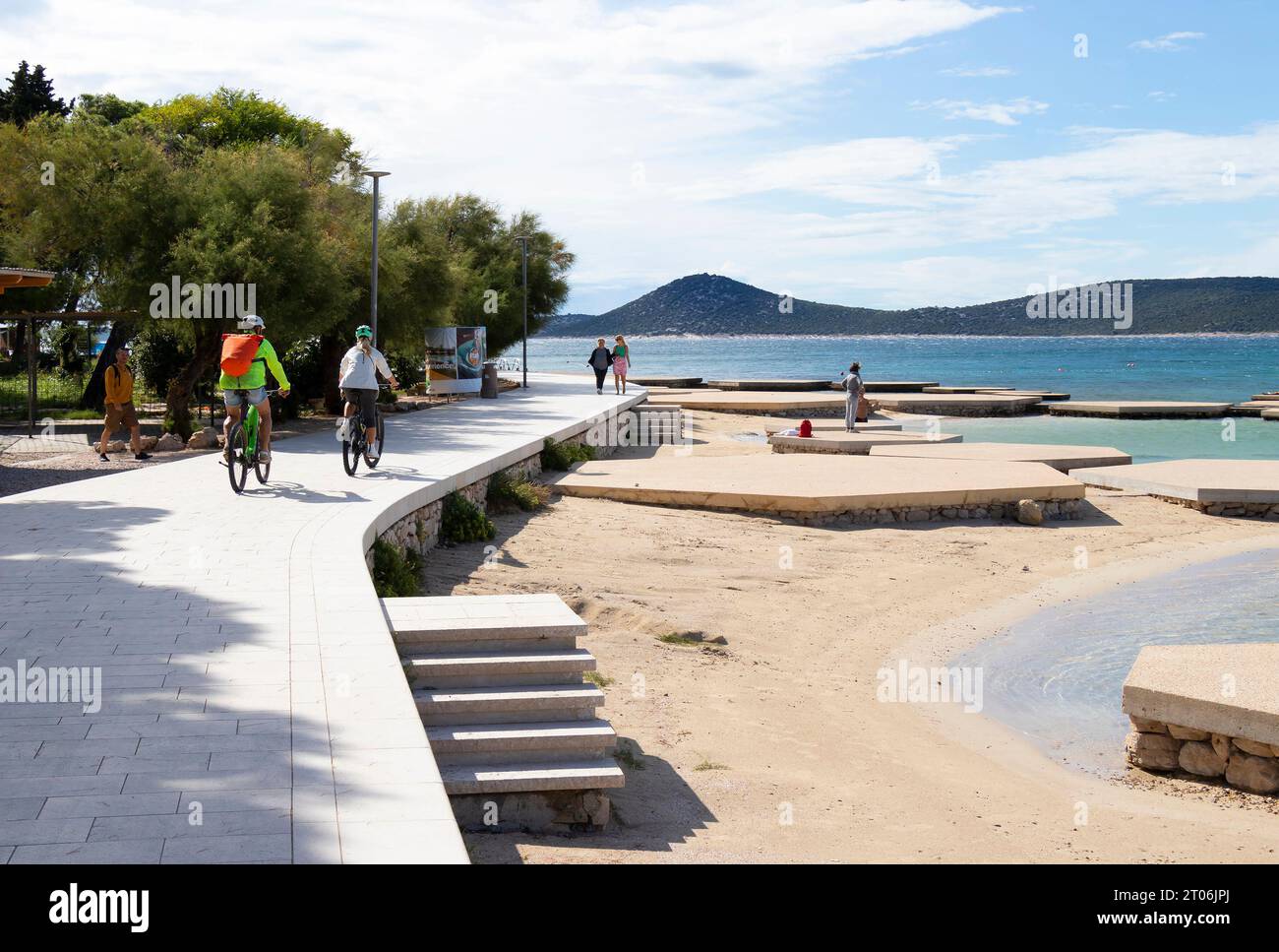 Vodice, Croatie - 24 septembre 2023 : les gens marchent et font du vélo sur la promenade près de la plage de bord de mer au coucher du soleil hors saison Banque D'Images