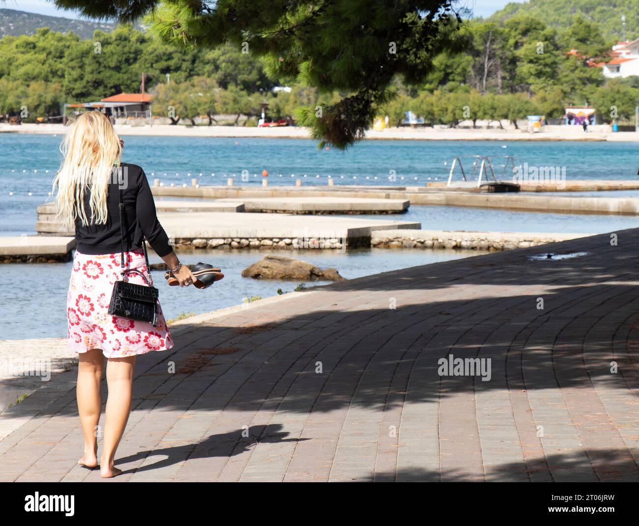 Vodice, Croatie - 24 septembre 2023 : Femme blonde marchant et faisant du vélo sur la promenade près de la plage au coucher du soleil hors saison Banque D'Images