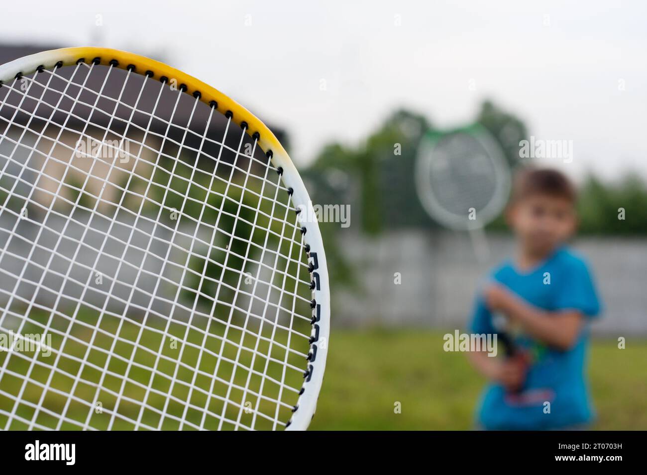 Portrait flou d'un enfant jouant au badminton dans l'arrière-cour de la maison. Loisirs d'été actifs pour enfants et adultes en plein air. Mode de vie sain. Sport Banque D'Images