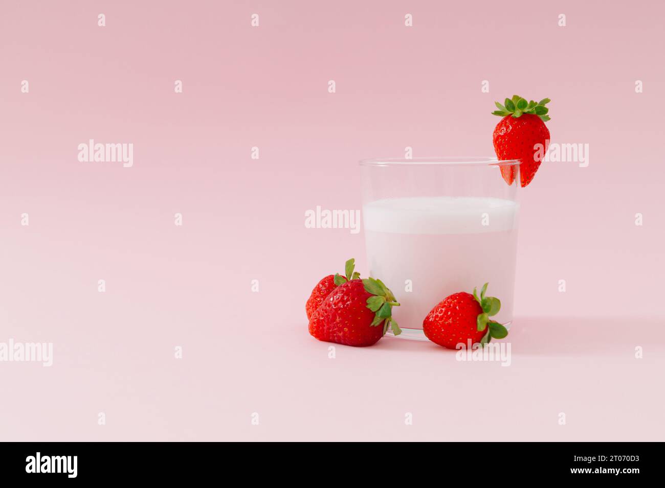 Composition créative à base de boisson au lait au goût de fraise dans une tasse en verre décorée de fraises rouges sur fond rose pastel. Concept minimal. Banque D'Images