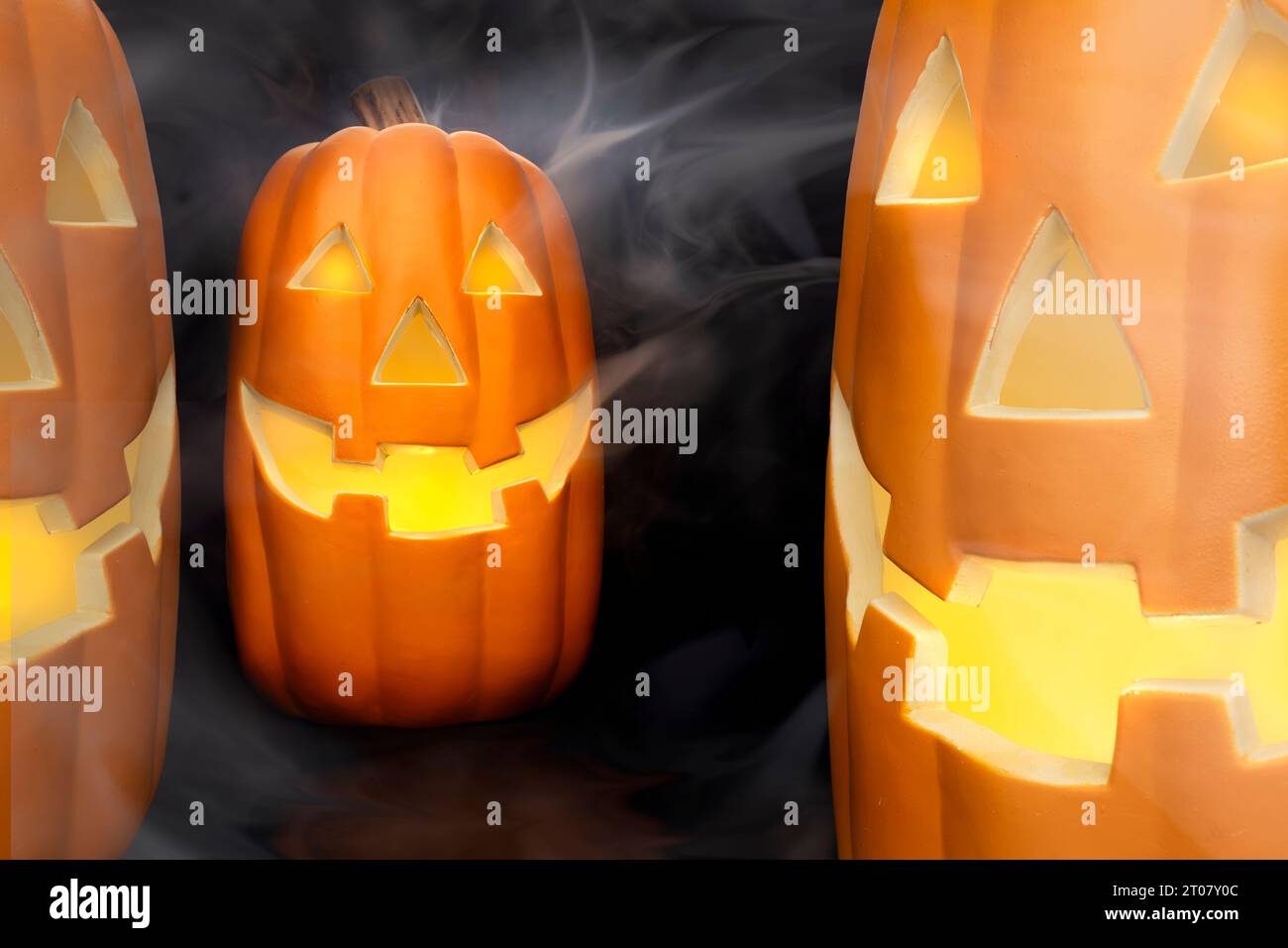 Citrouilles d'Halloween sculptées éclatantes avec brume fumée et visages effrayants sur un fond sombre. Banque D'Images