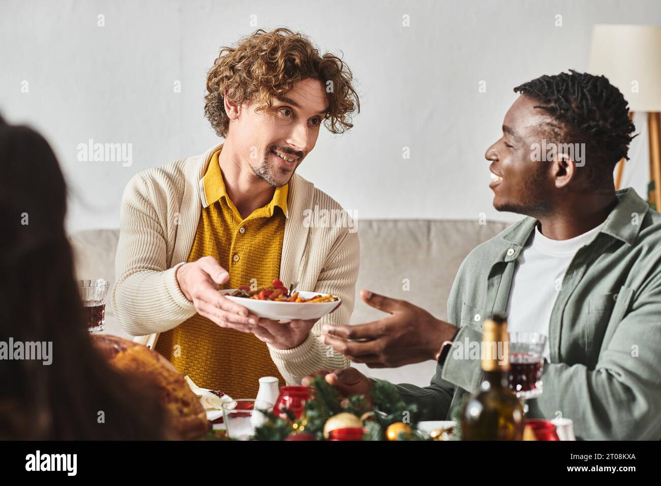 Jeunes parents multiculturels assis à table de vacances et partageant de la nourriture entre eux, Noël Banque D'Images
