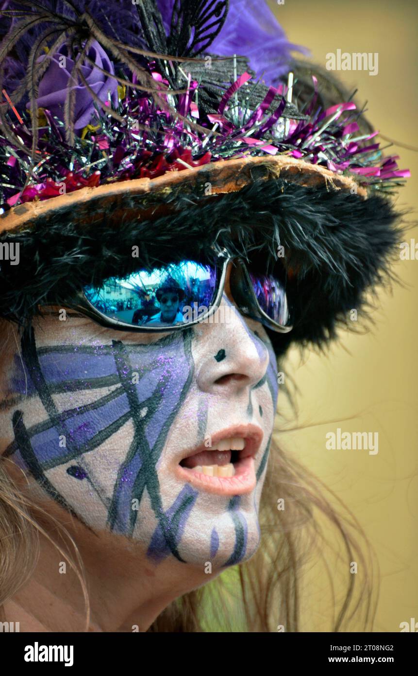 femme dans le chapeau de fantaisie et lunettes de soleil avec peinture de visage sur la bouche ouverte Banque D'Images