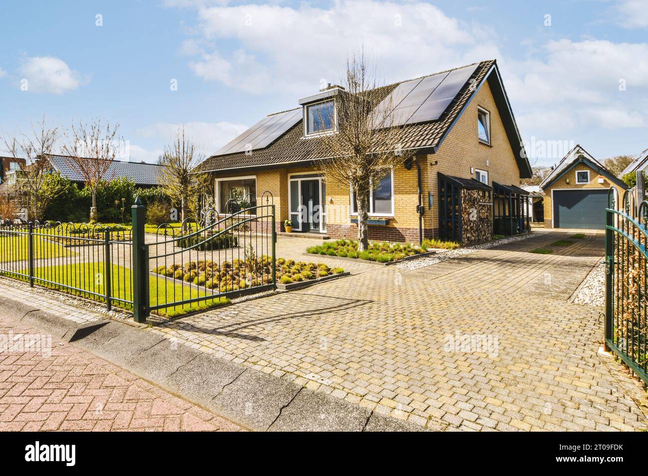 Façade de maison avec panneaux solaires sur le toit par allée pavestone et portail ouvert Banque D'Images