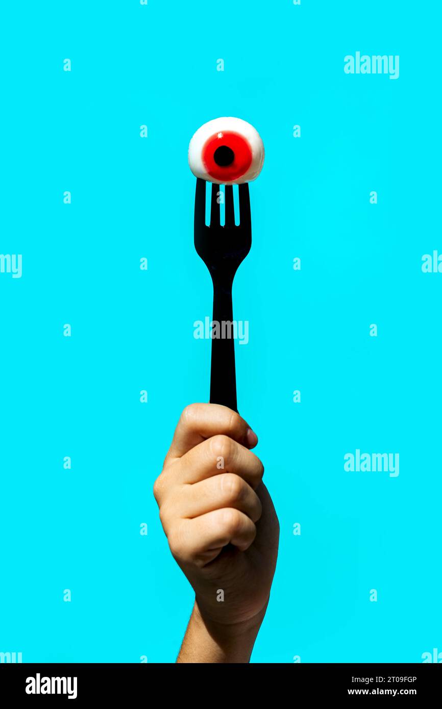 Main de la récolte anonyme personne tenant le globe oculaire avec l'iris rouge sur la fourche isolé sur fond bleu vif Banque D'Images