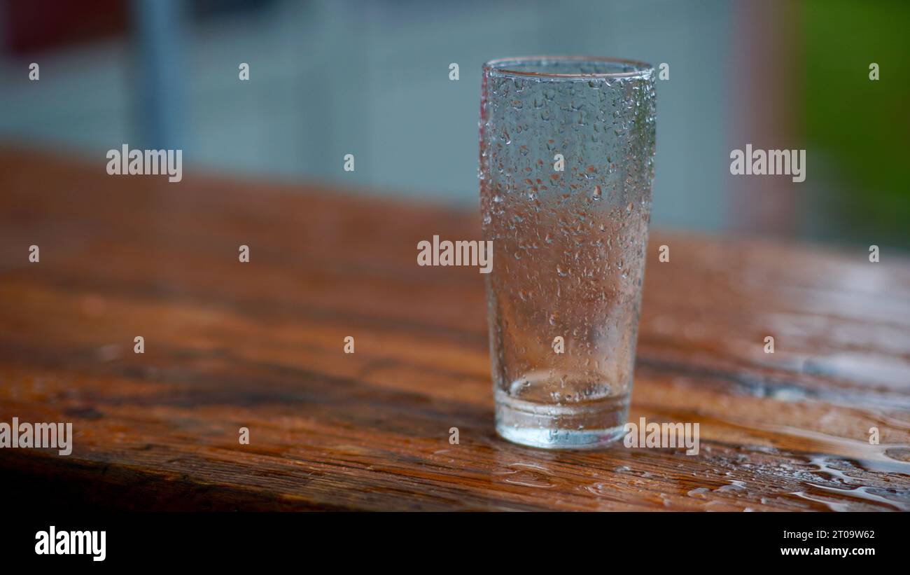 Un verre d'eau sur une table à bière sous la pluie. Banque D'Images